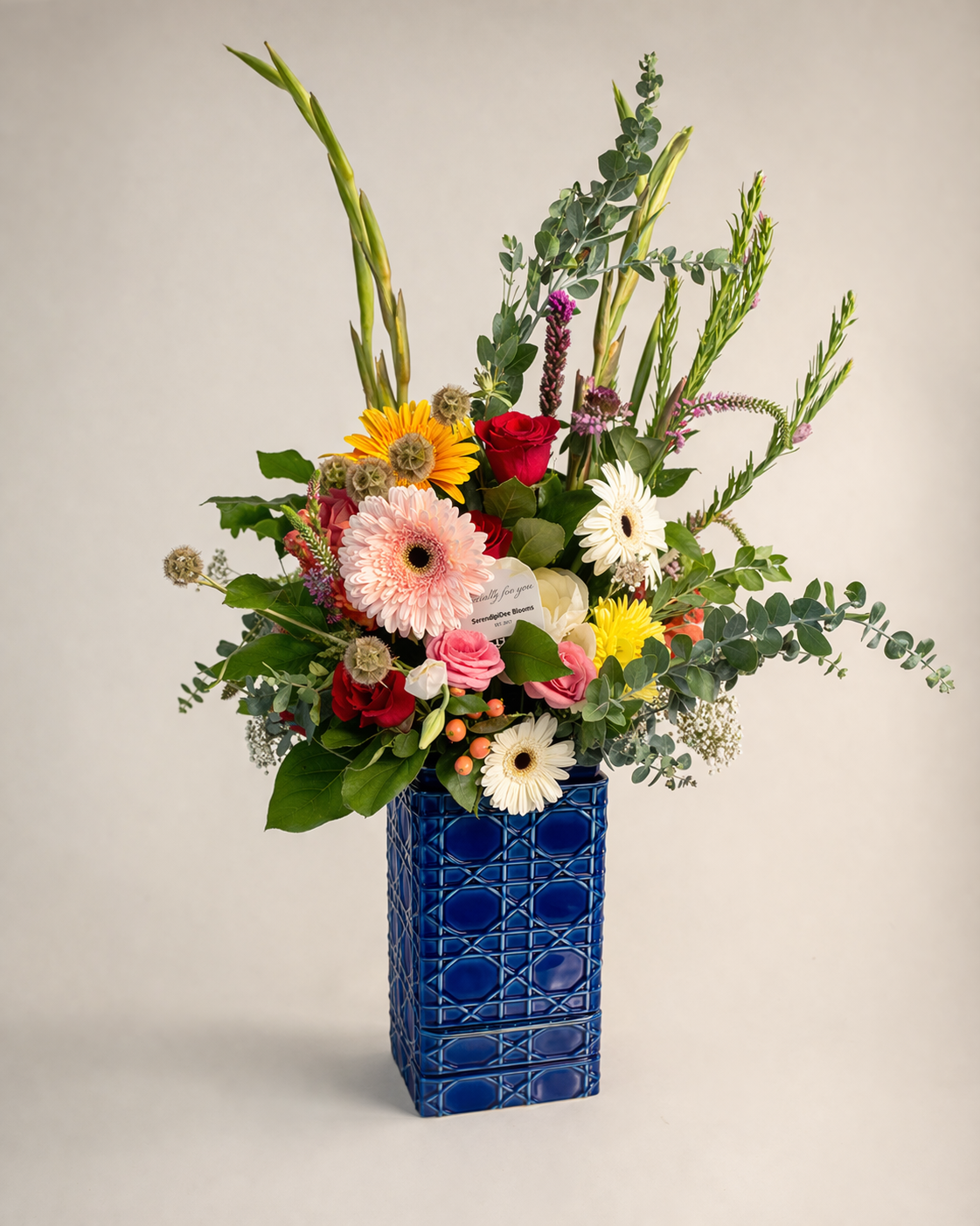 Tall mixed flower arrangement in a blue vase with gerbera daisies, roses, eucalyptus, and greenery, perfect for Mother’s Day gift.