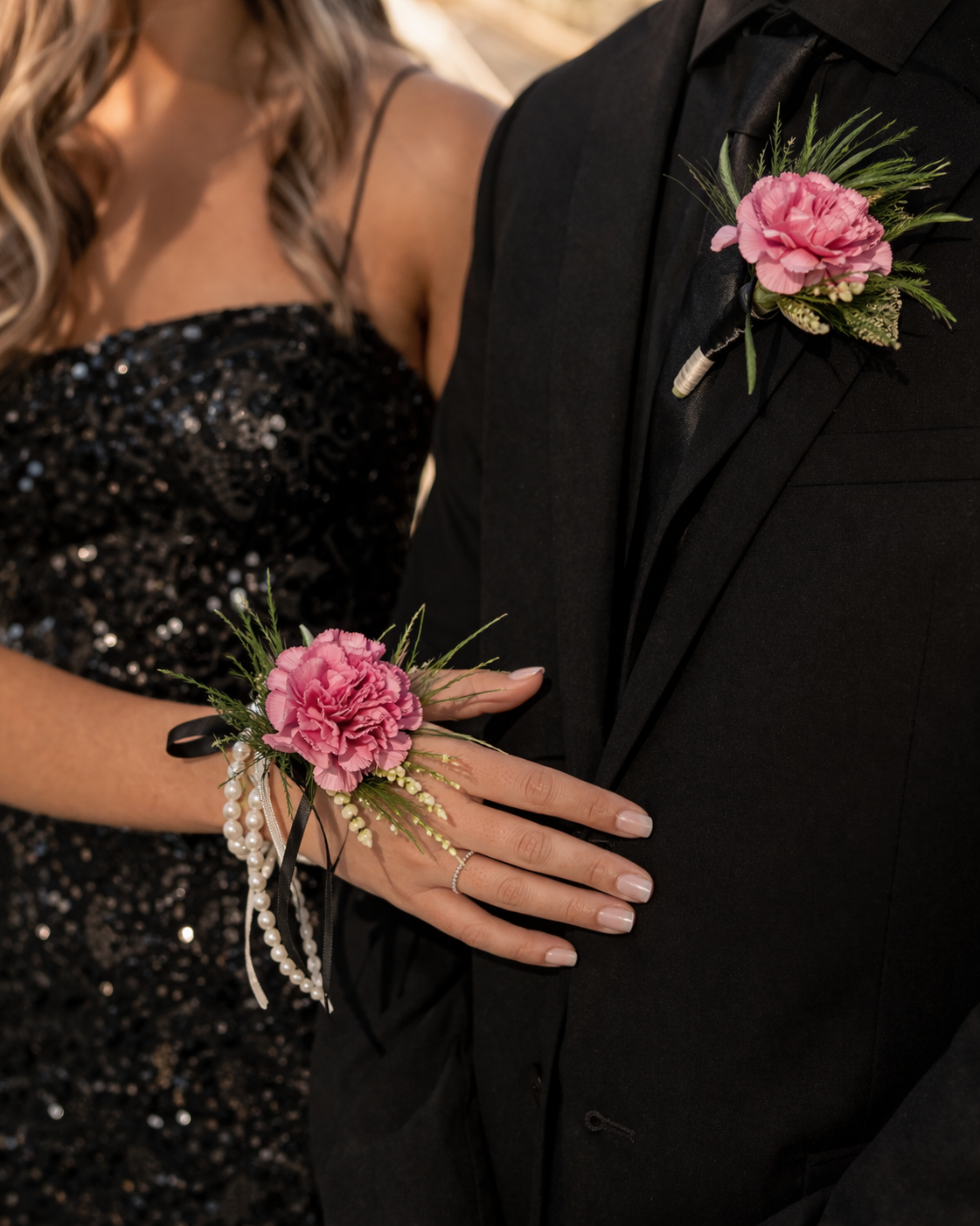 Prom corsage and boutonniere set from a Canonsburg, PA florist featuring pink flowers and greenery, styled on a wrist and black tuxedo