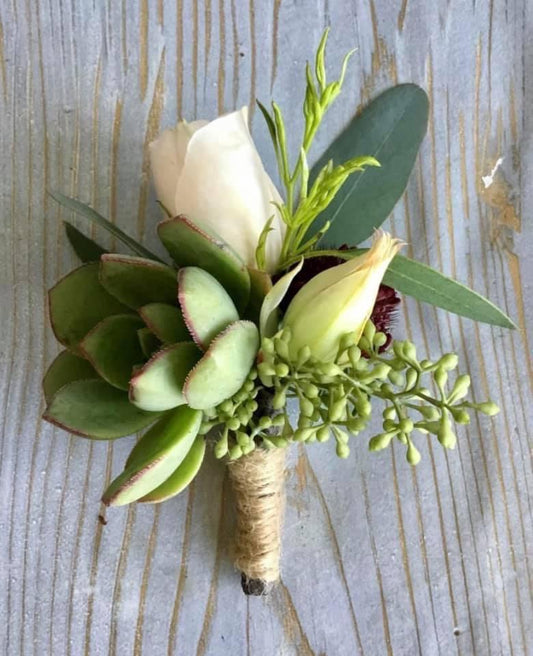 White and green boutonniere from a Canonsburg, PA florist featuring a white rose, succulent, and greenery on a rustic wood background